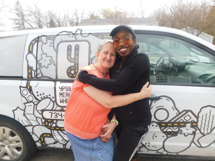 Two women hugging with Ypsi Meals on Wheels truck in background